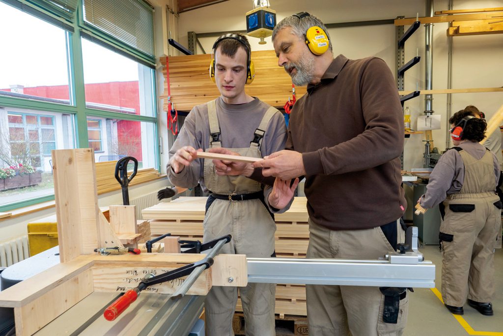 Ausbilder mit jungen Mann mit Beeinträchtigung in Holzwerkstatt